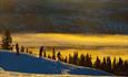 Snøbrettkjørere i varm vinterlys mot solnedgang i storslåtte omgivelser i Valdres Alpinsenter in Aurdal.