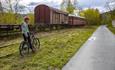 På gamle Bjørgo stasjon står fortsatt et gammelt togsett bestående av et lokomotiv og et par vogner på den gamle, gressbevokste skinnegangen. En syklist står foran toget med sykkelen sin.