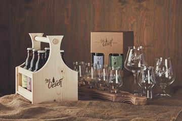 Eine Holzkiste mit Bierflaschen und verschiedene Biergläser, die auf groben Leinentuch dandiert sind.