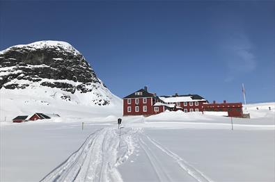 Bygdin Fjellhotell i vinterlandskap. Skiløype rett utenfor døra, og fjellet Bitihorn i bakgrunnen.