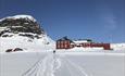 Rødt fjellhotell i vinterlandskap med løyper i for- og fjell i bakgrunnen