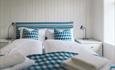 Ein Gästezimmer mit weißgestrichenem Holzpanel, einem weißen Bauernbett mit blau-weiß kariertem Bettbezügen.