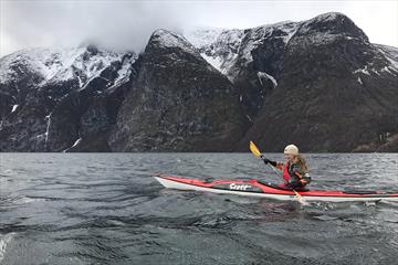 a kayaker on a fjord with snowy mountains in teh background