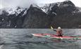 a kayaker on a fjord with snowy mountains in teh background