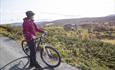 Cyclist standing next to her bike and taking in the view over idyllic mountain farm land