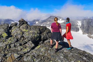 Two hikers at the summit cairn of a high mountain with view over a glacier towards mountains