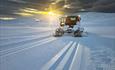Grooming machine grooming cross-country skiing tracks in mountains at sunrise