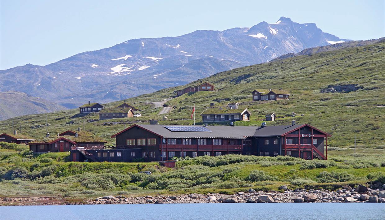 En fjellstue og et knippe hytter ved et vann i storslått høyfjellslandskap