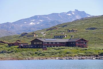 En fjellstue og et knippe hytter ved et vann i storslått høyfjellslandskap