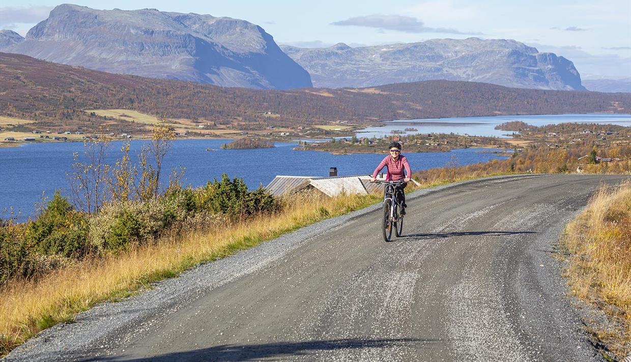 Syklist på grusvei med innsjøer og fjell i bakgrunnen