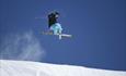 A skier jumps and crosses his skies. Blue skies in the backgound.