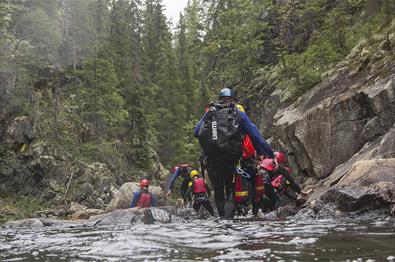 A group of persons with wetsuits and helmets walks in a river.