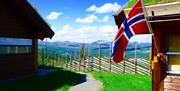 Flott naturbilde med norsk flagg, litt av hyttene og flotte fjellpartier i bakgrunnen.