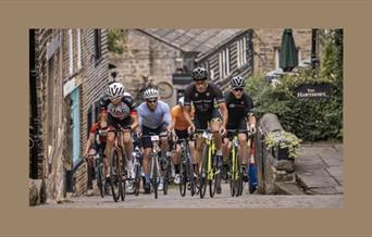 A picture of a group of competitive cyclists, riding up a cobbled village street