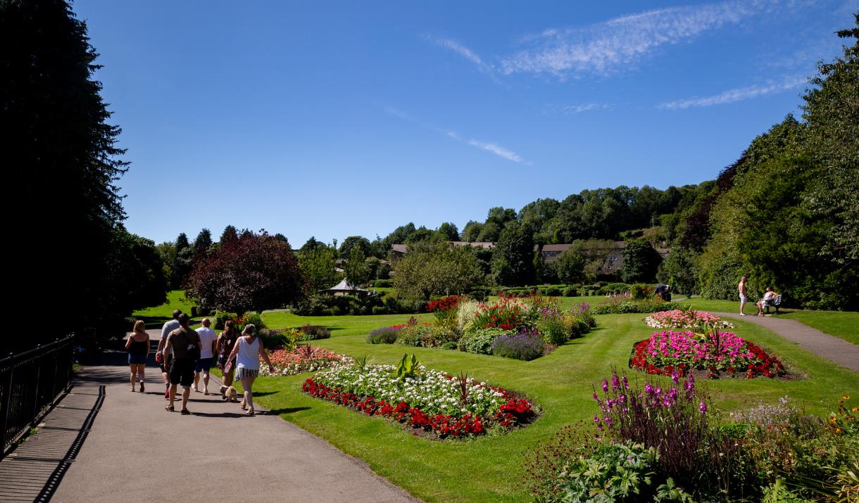 On a sunny summer day in Haworth Central Park, there is a clear sky and lovely flowerbeds.