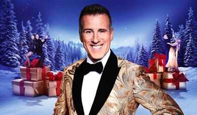 A picture showing Anton Du Beke in the foreground, with two pairs of dancers in the background, all set against a nighttime snowy forest
