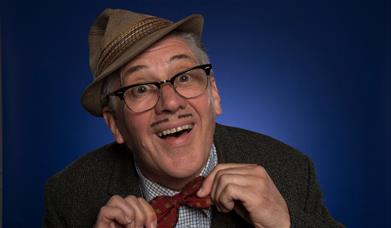 A picture of the character Count Arthur Strong, wearing his trilby at a jaunty angle, and smiling 