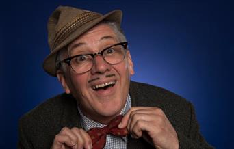 A picture of the character Count Arthur Strong, wearing his trilby at a jaunty angle, and smiling