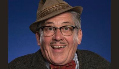 A picture of the character Count Arthur Strong, wearing his trilby at a jaunty angle, and smiling 