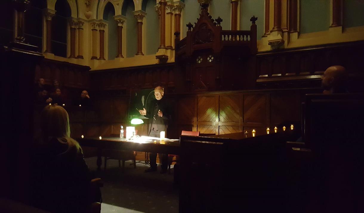 The courtroom in City Hall, in darkness, with a speaker lit by lamplight.