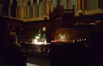 The courtroom in City Hall, in darkness, with a speaker lit by lamplight.