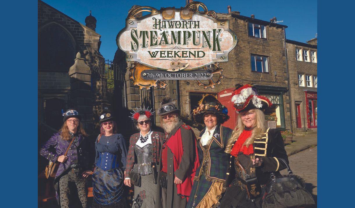 A picture of six people on steampunk costumes, standing together in front of shops on a cobbled street