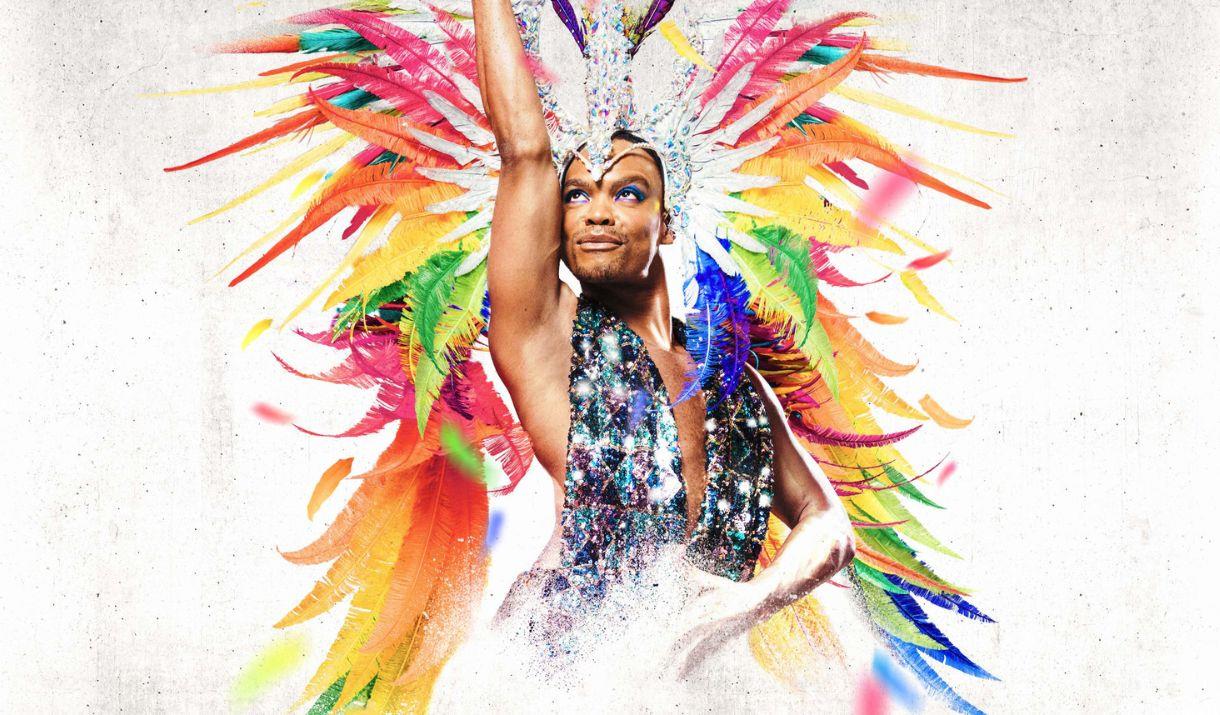 A photograph of dancer Johannes Radebe, in a glittery costume and headdress with rainbow feathers