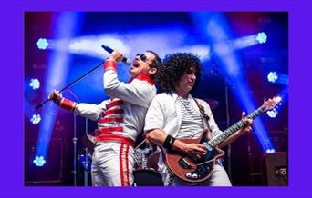 A photograph of two of the members of the Magic! Queen tribute act on stage - "Freddy Mercury" and "Brian May"