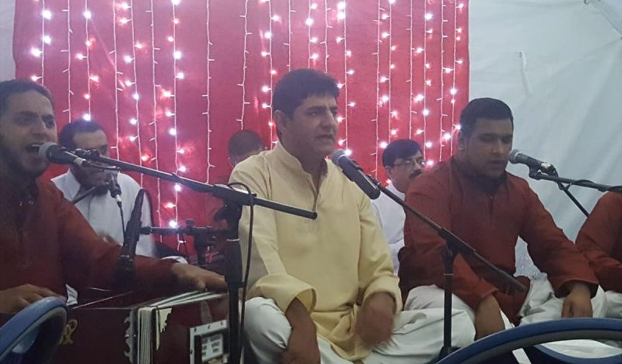 A picture of a group of qawwali musicians, sitting on the floor, playing instruments and singing