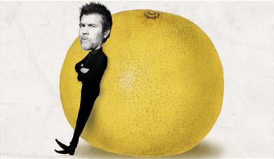 A picture of comedian Rhod Gilbert. leaning against a giant grapefruit