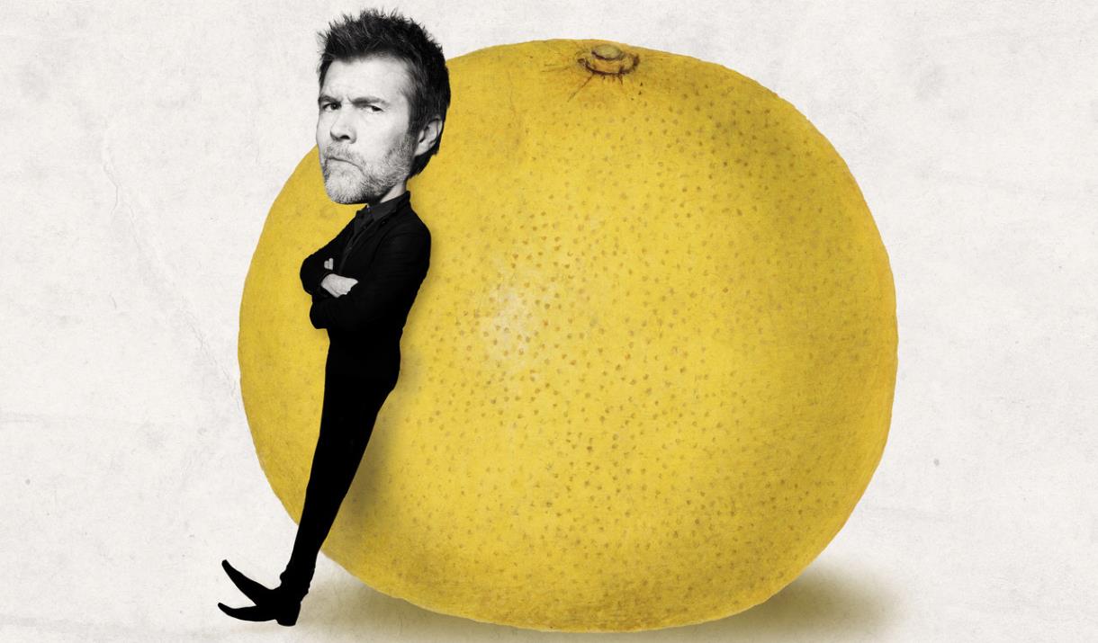 A picture of comedian Rhod Gilbert. leaning against a giant grapefruit