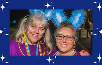A picture of two women wearing blue and white bunny ears, face paint and colourful beads