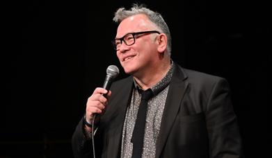 A photograph of comedian Stewart Lee, holding a microphone
