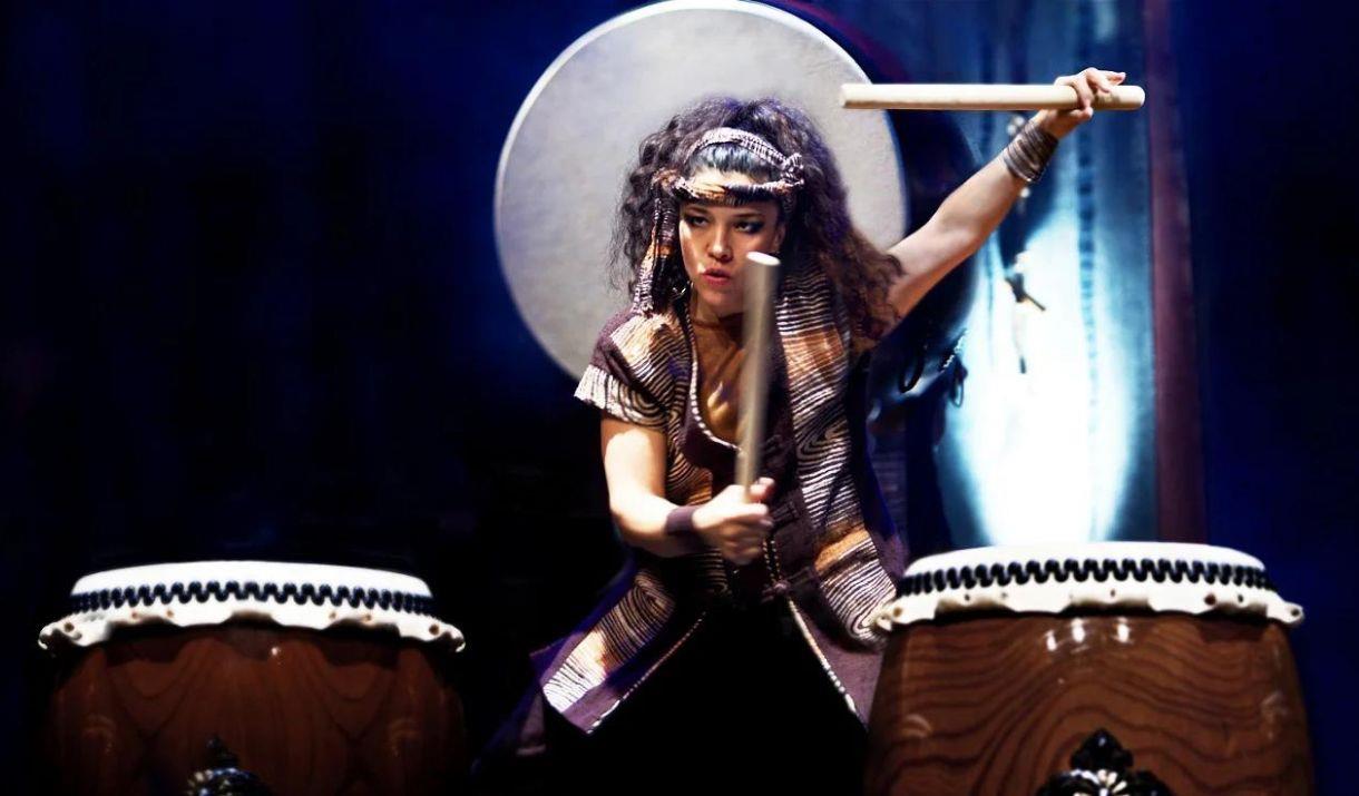 A photograph of a woman holding two large drum beaters above two large Japanese Taiko drums