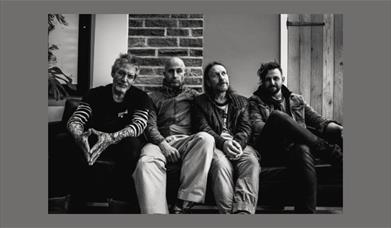 A black and white photograph of the rock band Terrorvision, sitting on a sofa