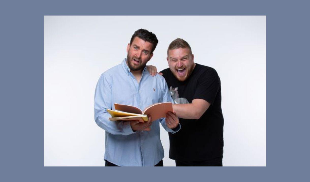 A picture of two men, looking at some exercise books. One is laughing, and the other looks puzzled
