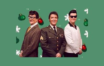 Three men standing together, facing forward, and smiling. One is dressed as Buddy Holly, one as Elvis, and one as Roy Orbison
