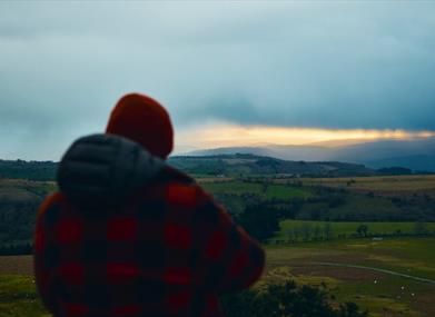 A walker in a red check jacket looking over the valley at dusk