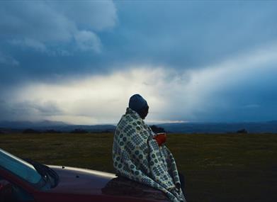 A person wrapped in a Welsh wool blanket holding a warm mug at dusk