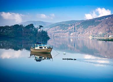 A small boat on the still Mawddach river at Penmaenpool with woods on the hillside