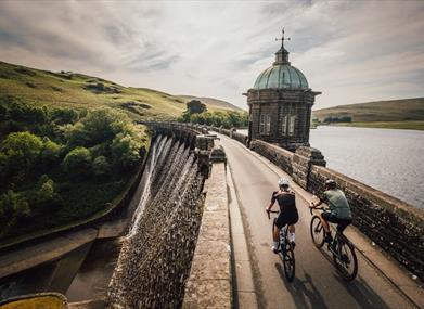 Cyclists riding across the top of a Victorian dam in the Elan Valley with water pouring over the side