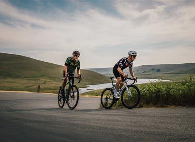 Two road cyclists riding side by side above a reservoir in the Elan Valley
