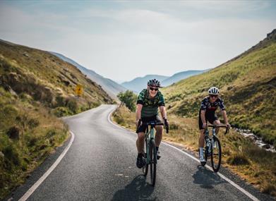 Two cyclists riding towards the camera on a mountain road through a green valley in Mid Wales