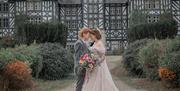 Two women in wedding outfits in front of a black and white stately home