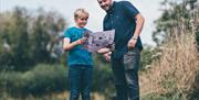 A father and son are standing in the wildflower meadow looking at a map.