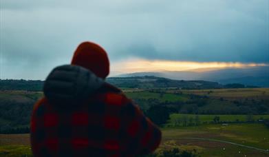 A walker in a red check jacket looking over the valley at dusk