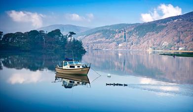 A small boat on the still Mawddach river at Penmaenpool with autumn woods on the hillside