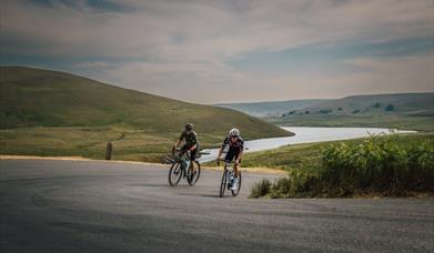Two cyclists on an open road above a river valley in the hills of Mid Wales