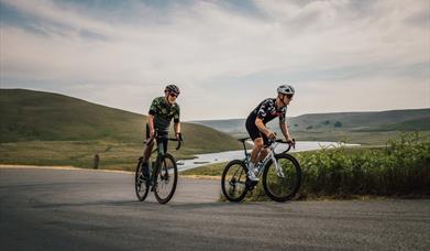 Two road cyclists riding side by side above a reservoir in the Elan Valley