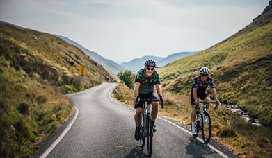 Two cyclists riding towards the camera on a mountain road through a green valley in Mid Wales